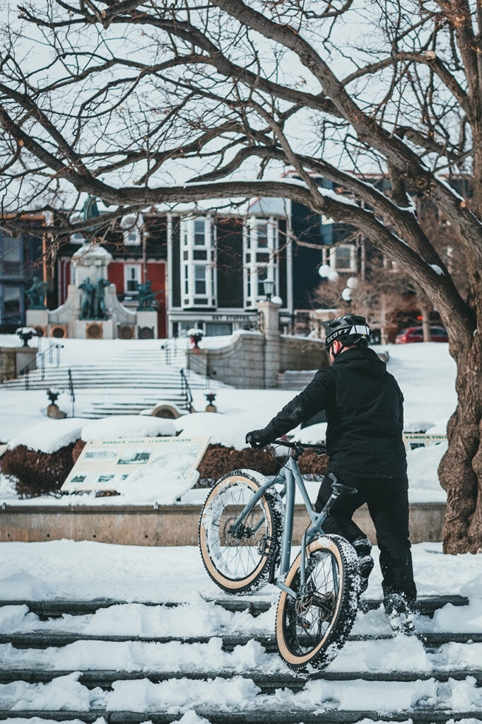 man pulling mountain bike up snowy steps to ride to work